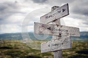 Recycle, reduce and reuse text on wooden sign post outdoors in landscape scenery.