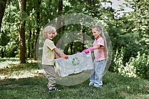 Recycling concept. Two cute little boy and girl holding recycle bin with plastic waste while standing in the forest or