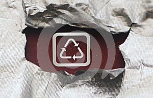 Recycling icon symbol in silver on dark red under torn foil paper. Eco healthy living reuse reduce concept