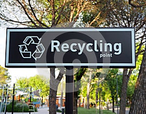 Recycling point sign ,words and symbol in white color on black background. Blurred public park on behind