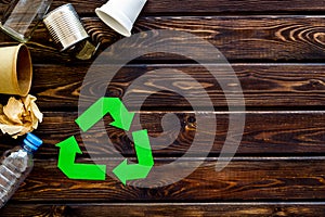 Recycling sign with waste materials, bottle, cups, can for ecology concept on wooden background top view mock up