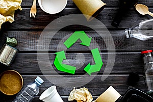 Recycling symbol and different garbage, paper cup, flatware, plastic bottle, can for ecology wooden background top view