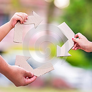 Recycling symbol People`s hands hold the symbol of an arrow in a paper hard box.