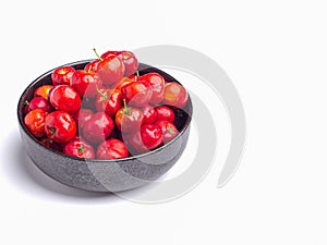 Red acerola cherries fruit in a ceramic bowl isolated on a white background.