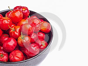 Red acerola cherries fruit in a ceramic bowl isolated on a white background.