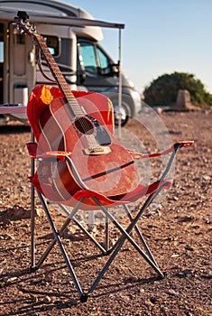Red acoustic guitar on a folding chair near camper