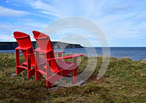 Red Adirondack chairs on the edge of a cliff overlooking the ocean
