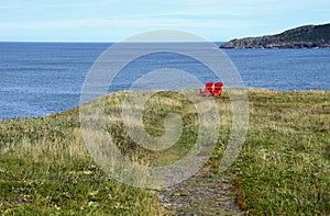 Red Adirondack chairs on the edge of a cliff overlooking the ocean