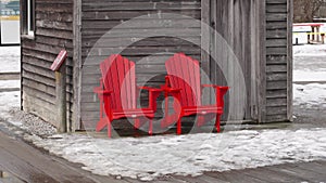 Red Adirondack Chairs in Winter by Rustic Wooden Cabin