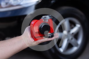 Red air horn for a car on men`s hand before a modern black car. Electric Car air horn.