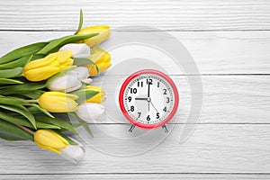 Red alarm clock and beautiful tulips on white wooden table, flat lay with space for text. Spring time