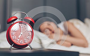 Red Alarm clock on bedside table with Woman sleeping on background.