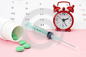 Red alarm clock, a calenar, syringe and pills.