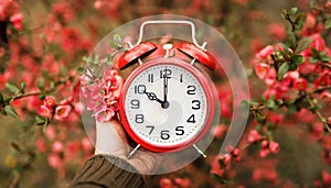 Red alarm clock in flowers in spring, daylight savings time banner or background