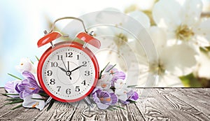 Red alarm clock and flowers on table against background, space for text. Spring time