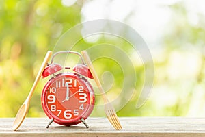 Red alarm clock, Fork, and spoon on wooden table with green outdoor nature blur background. Eight o'clock, Time for eating concep
