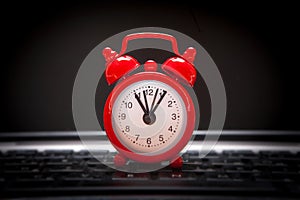 Red alarm clock lies on the laptop keyboard