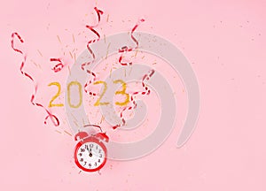 Red alarm clock on  pink background with confetti and gold serpentine
