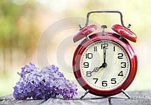 Red alarm clock and purple flower, daylight savings time, spring forward concept