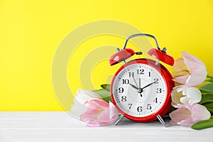 Red alarm clock and spring flowers on background, space for text. Time change