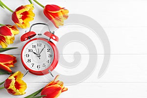 Red alarm clock, spring flowers and space for text on wooden table, flat lay. Time change