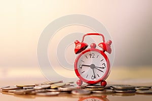 Red alarm clock on stack of coins in concept of savings and money growing or energy save.