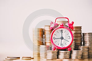 Red alarm clock on stack of coins in concept of savings and money growing or energy save.