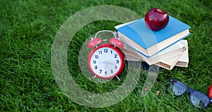 Red Alarm clock and stack old books in park in autumn morning, concept of education and reading. Books, apple, glasses with an ala