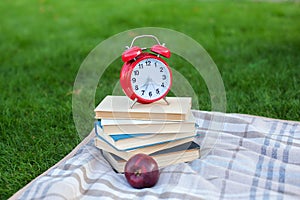 Red Alarm clock and stack old books in park in autumn morning, concept of education and reading. Books, apple with an alarmclock l