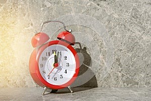 Red alarm clock with a sunlight and shadow on the grey stone background