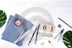 Red alarm clock and supplies, wooden calendar with date 1st September. on white desk. Back to school concept.