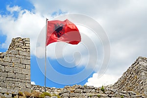 Red Albanian flag with double-headed black eagle waving over wall of Fortress Rozafa near Shkodra city. Fluttering banner with