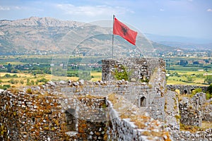 Red Albanian flag with double-headed black eagle waving over wall of Fortress Rozafa near Shkodra city. Fluttering banner with