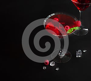 Red alcohol raspberry cocktails in martini glass with mint on the black background. Copy space. Selective focus.