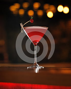 Red alcoholic cocktail decorated with berry at wooden table. Transparent glass of alcoholic drink isolated on black