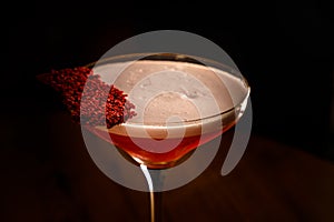 A red alcoholic cocktail with foam in a glass stands on the bar