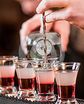 Red alcoholic drink in glasses on bar. Red cocktail at the nightclub. Barman preparing cocktail shooter. Bartender