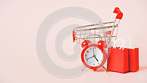 Red analog alarm clock, shopping bag and blurred shopping cart, sale or promotion, business background