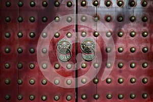 Red antique Chinese doors with brass lion head door knockers and gilded studs.