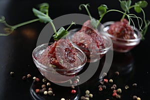 Red appetizing Tartar sauce in three pialas, decorated with a stem of sprouted green peas, close-up