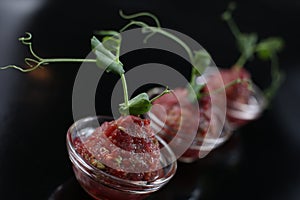 Red appetizing Tartar sauce in three pialas, decorated with a stem of sprouted green peas, close-up