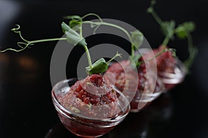 Red appetizing Tartar sauce in three pialas, decorated with a stem of sprouted green peas, close-up