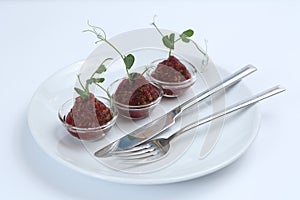 Red appetizing Tartar sauce in three pialas on a plate with a knife and fork, decorated with a stem of sprouted green peas, close-
