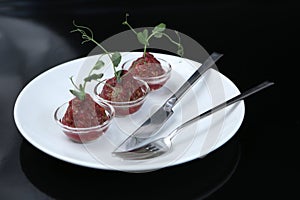 Red appetizing Tartar sauce in three pialas on a plate with a knife and fork, decorated with a stem of sprouted green peas, close-