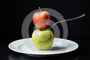 A red apple balanced on a fork above a green apple.