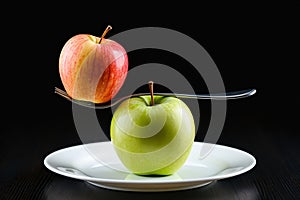 A red apple balanced on a fork above a green apple.