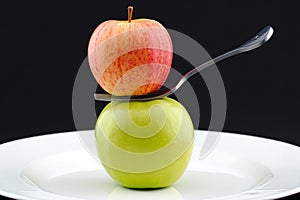 A red apple balanced on a fork above a green apple.