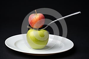 A red apple balanced on a fork above a green apple.