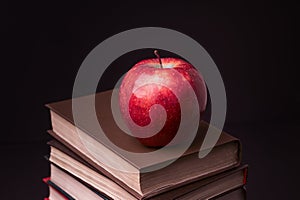 Red apple on book stack on black background