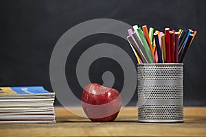 Red apple, books and penciles on wooden table and blackdoard background.school for kids